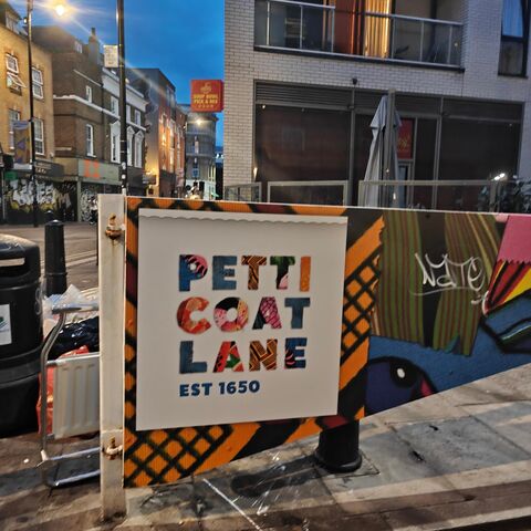 The Petticoat Lane market sign at dusk, against a painted hoarding in east London.